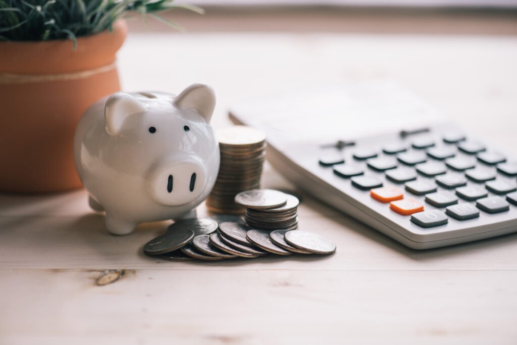 Piggy,Banks,Standing,Among,Pile,Of,Coins,And,Calculator.
